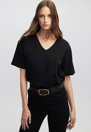 Camiseta negra de pico con mangas cortas, hecha de algodón suave, combinada con pantalones negros de cintura alta y un cinturón negro con hebilla dorada.