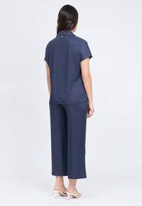 Top corto blu navy con colletto, maniche corte e dettagli sul retro. Abbinato a pantaloni a gamba larga coordinati, entrambi realizzati in un tessuto morbido e liscio.