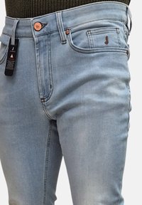 Jeans in denim azzurro chiaro con vestibilità slim, caratterizzati da una vita con bottone di rame e un'etichetta visibile sulla tasca anteriore.