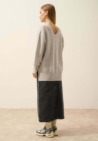 Lichtgrijze gebreide trui met een V-hals, gedragen over een lange zwarte spijkerrok. Gecombineerd met grijze sneakers en crèmekleurige sokken.