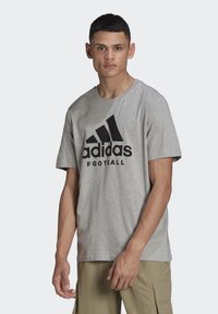 T-shirt in cotone grigio con scollo rotondo, caratterizzato da un grande logo Adidas nero e la scritta "Football" stampata sul davanti.
