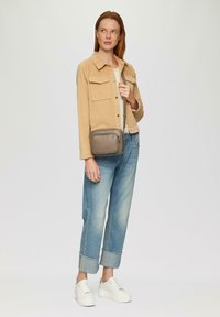 Beige Cordjacke mit zwei Brusttaschen, hellbeiges Oberteil, lockere blaue Jeans mit hochgerollten Säumen, weiße Plateausneaker und graue Umhängetasche.