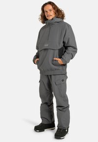 Szary sweter z półzamkiem, kieszenią z przodu i elastycznymi mankietami, w połączeniu z pasującymi spodniami cargo, które mają kieszenie boczne i luźny krój.