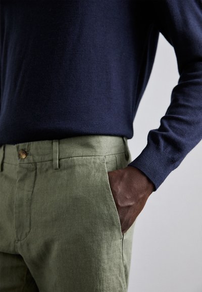 Marineblauw sweater met lange mouwen, gecombineerd met lichtgewicht, lichtgroene linnen broek met een voorzak en een knoopdetail.