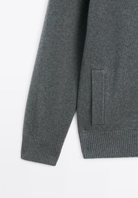 Pull en maille gris foncé à manches longues avec poignets, ourlet côtelés et poche verticale sur le côté droit.