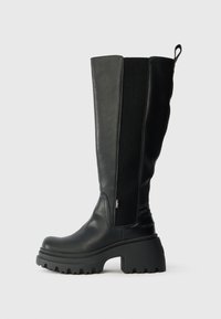 Černé kožené vysoké boty až ke kolenům s texturovanou panely, silnou platformou a poutkem na zadní části pro snadné oblečení.