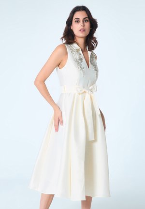 Une robe blanche sans manches avec un corsage ajusté, un col brodé, une large ceinture à la taille et une jupe évasée, arborant des accents jaune pâle.