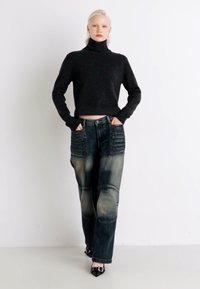 Sweater preto de gola alta cropped e jeans de ganga rasgados de cintura alta com detalhes em nervuras, apresentando uma palete de cores azul e verde desgastada.