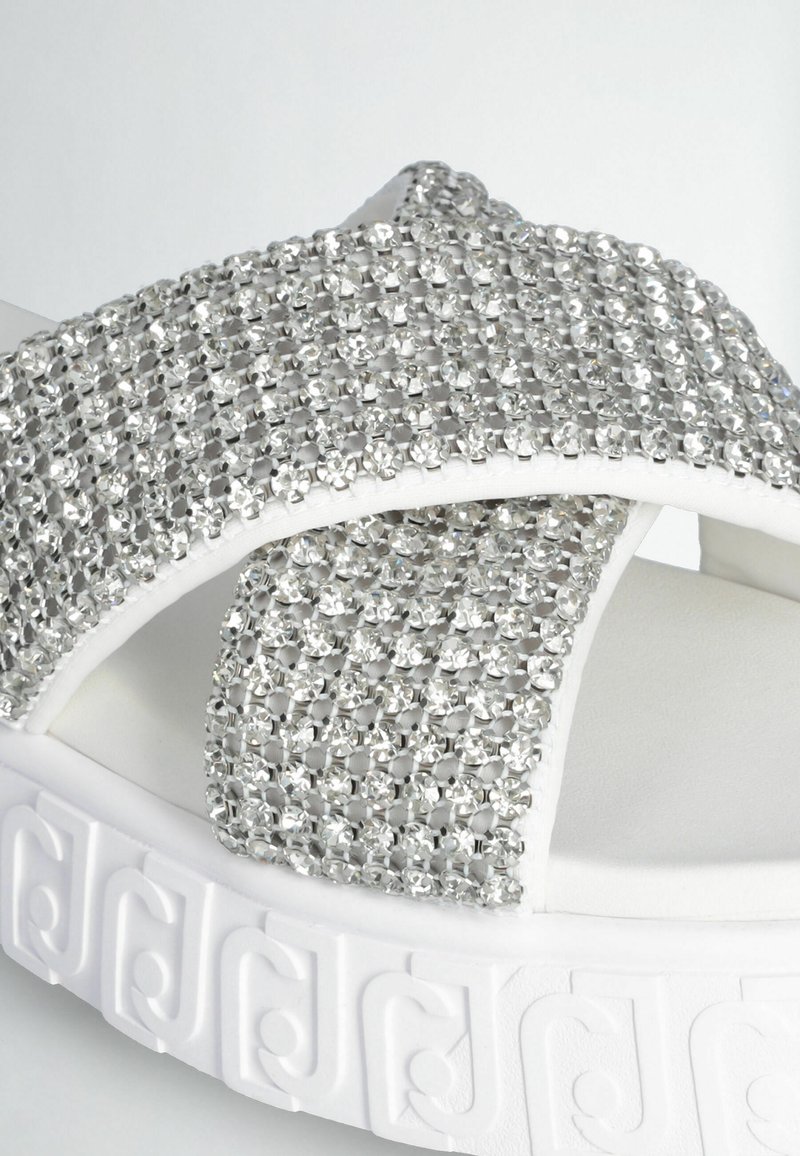 Sandali platform bianchi con suola testurizzata, dotati di una fascetta incrociata decorata con strass argentati per un tocco di brillantezza.