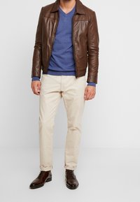 Brązowa skórzana kurtka, niebieski sweter, beżowe spodnie i ciemnobrązowe buty. Strój charakteryzuje się nowoczesnym krojem z eleganckim designem i czystymi liniami.