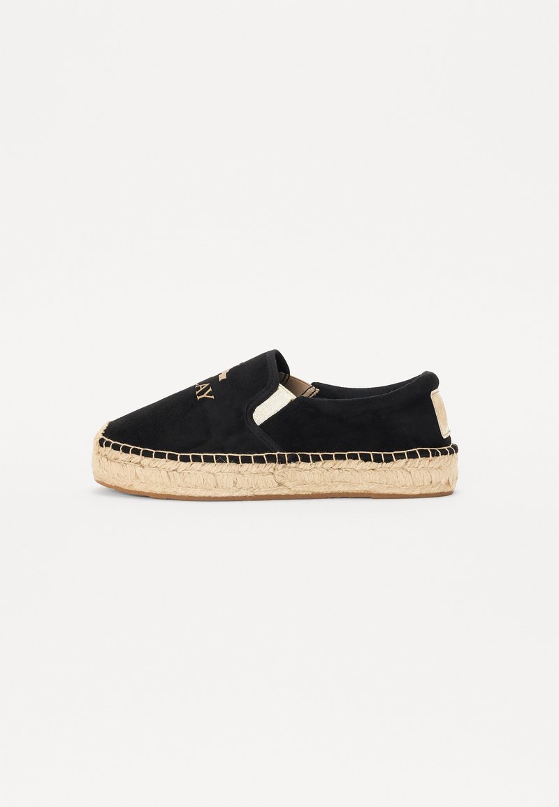 Espadrille noire à enfiler avec semelle en jute tissée beige et détails cousus, comportant des lettres dorées sur la partie supérieure.