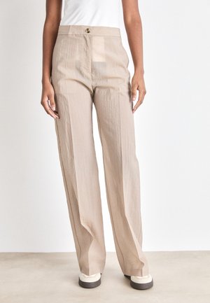 Beige wijde broek met een licht gekreukt textuur, hoge taille en een enkele voorknop. Gepaard met lichtgekleurde sneakers.
