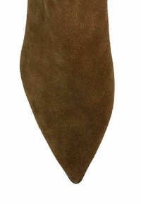 Chaussure en daim marron à bout pointu avec une texture lisse et un design épuré, se rétrécissant en une pointe aiguë, soulignant une silhouette élégante.