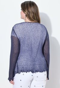 Blå, texturerad stickad tröja med vågig nederkant och långa ärmar. Genomskinlig tyg skapar en lager-på-lager-look. Buren över ljusa byxor med hjärt-mönster.