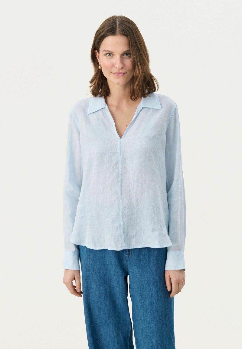 Camicia in lino azzurro chiaro con colletto a punte, maniche lunghe e vestibilità rilassata. Presenta una trama sottile e un dettaglio con patta sul fronte.