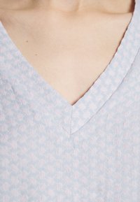 Jasnoniebieska, fakturowana tkanina z delikatnym wzorem, posiadająca dekolt w serek oraz miękką, tkana strukturę. Brak widocznych elementów metalowych lub akcentów.