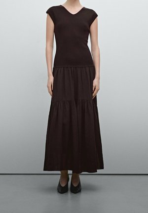 Black dress with a fitted top and a tiered, flowing skirt. Short cap sleeves, V-neckline, and a soft texture. Worn with black shoes.