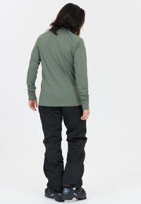 Langemouwen, T-shirt met ronde hals in olijfgroen met subtiele stikdetails, gecombineerd met lose zwarte broeken en zwarte skistokken.