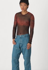 Top de manga longa em malha na cor vermelho escuro e preto. Combinado com calças largas em denim azul com bolsos frontais e detalhes nas costuras.