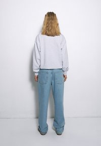 Jasnoszara, oversize bluza z długim rękawem, zestawiona z jasnoniebieskimi spodniami typu wide-leg, o minimalistycznym wzornictwie i bez widocznych wzorów.