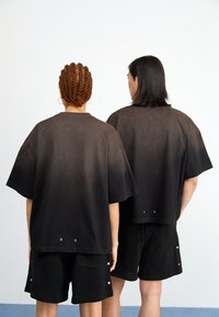 Juodos medvilnės mišinio pernelyg didelės t-shirt su gradientiniu išblukimu, derinamos su juodomis tekstūruotomis šortais, turinčiais mygtukus ir užpakalines kišenes.