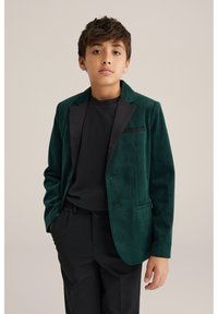 Grön sammetsblazer med svarta satinfickor, enkelknäppt stängning och sidofickor, kombinerad med en svart skjorta och byxor.