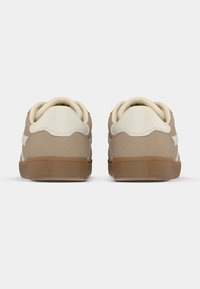 Μπεζ αθλητικά παπούτσια με λεία υφή, λευκές λεπτομέρειες, στρογγυλεμένη φτέρνα και λαστιχένια σόλα, με ραφές σε τόνους κατά μήκος της πίσω πλευράς.
