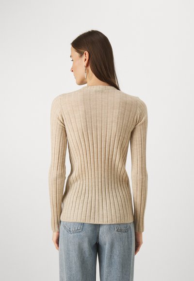 Pull à côtes beige à manches longues, col rond et coupe ajustée, associé à un jean taille haute bleu clair.