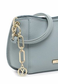 Bolso de piel azul claro con forma redondeada, que cuenta con un acento de cadena dorada y un charm circular. Acabado texturizado y asas superiores.