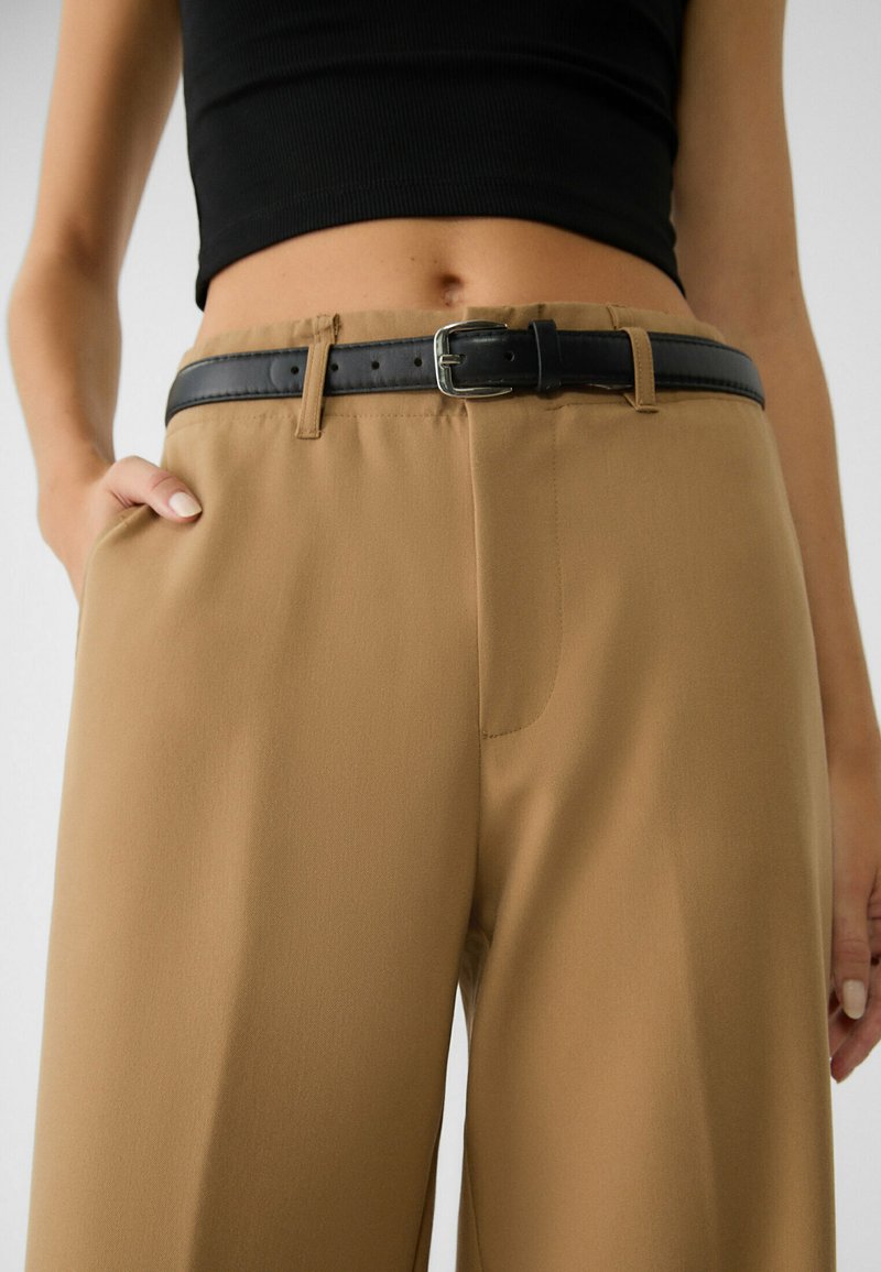 Pantaloni marroni realizzati in tessuto morbido con una vestibilità rilassata, dotati di una cintura nera con fibbia in metallo e tasche laterali.