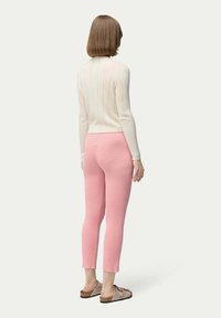 Ribbade krämfärgade långärmade toppar med en figurnära silhuett, parat med ljusrosa, korta ribbade leggings och beige slide-sandaler.
