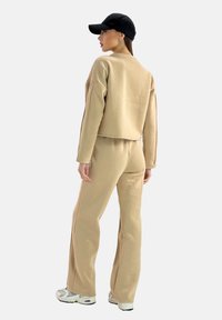 Felpa beige a cropped e pantaloni ampi abbinati realizzati in morbido tessuto, abbinati a un berretto nero e sneakers bianche.