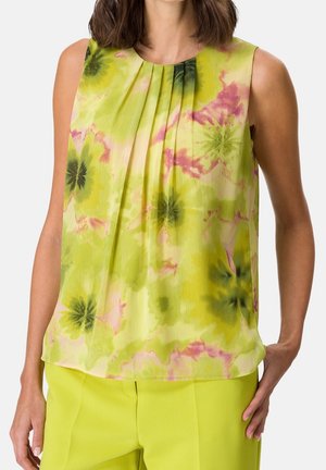Blouse sans manches avec un motif floral tie-dye en vert clair, vert foncé et rose, associée à un pantalon jaune-vert vif.