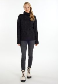 Schwarzer gestrickter Rollkragenpullover mit Zopfmuster, gerippten Bündchen und Saum, kombiniert mit dunkelgrauen Skinny-Jeans und cremefarbenen Schnürstiefeln.