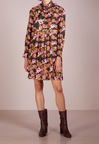 Abito floreale di colore verde scuro, con fiori rosa e arancioni, colletto arricciato, maniche lunghe e gonna plissè. Stivali con tacco marroni.