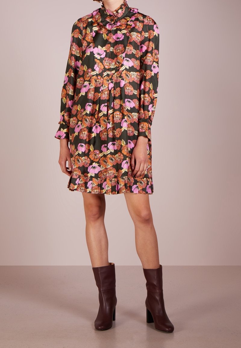 Abito floreale di colore verde scuro, con fiori rosa e arancioni, colletto arricciato, maniche lunghe e gonna plissè. Stivali con tacco marroni.