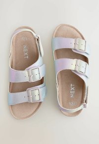 Sandali iridescenti con due fibbie regolabili, suola piatta e interno morbido simile al suede, in tonalità di rosa e blu pastello.