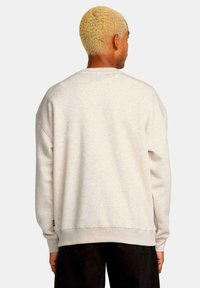 Sudadera de gran tamaño en gris claro con cuello redondo y hombros caídos. Puños y dobladillo acanalados, con una pequeña etiqueta de la marca en el lateral.