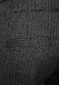 Grå herringbone-mönstrade byxor med en elegant, avsmalnad design och en bakficka med horisontell öppning.