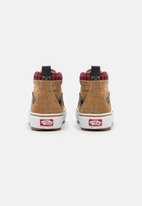 Sneakers înalte din suede maro cu accente negre și un guler din carouri roșii, având tălpi albe și un logo roșu pe călcâi.