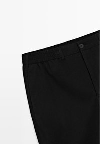Zwarte broek met een elastische tailleband, enkele knoopsluiting en een gladde stof met zijzakken, in een schuine aanzicht.
