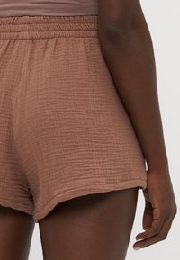 Shorts marron texturés avec une coupe décontractée et une taille élastique, présentant un motif à carreaux subtil et un ourlet roulé.