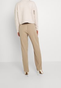 Béžové kalhoty s vysokým pasem a hladkým povrchem, s tapered nohavicemi. V kombinaci s lehkým pleteným svetrem s krátkým střihem.