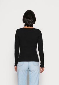 Pull noir ajusté à côtes avec des manches longues et un décolleté carrément, porté avec un jean taille haute bleu clair. Design simple, sans motifs.