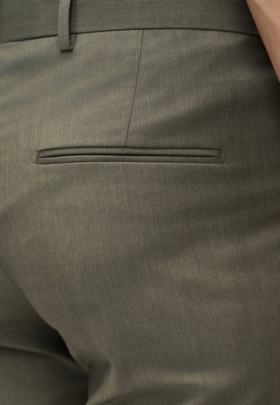 Κοντινό πλάνο ελιάς-πράσινου παντελονιού, ραμμένο, που δείχνει μια πίσω τσέπη με άνοιγμα και λεπτομέρεια θηλιάς ζώνης στη μέση.