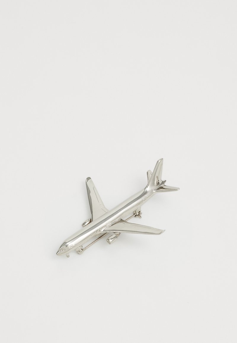Insigna de avion din metal argintiu cu aripi și motoare detaliate pe un fundal alb simplu.