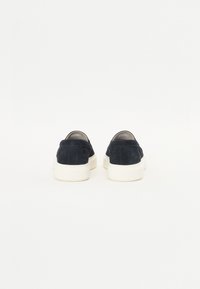Scarpe slip-on in suede di colore blu navy con una suola in gomma bianca spessa e dettagli di cucitura minimi, caratterizzate da un tallone arrotondato e una superficie liscia.