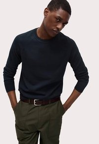 Námořnický svetr s kulatým výstřihem z texturované látky, kombinovaný s olivově zelenými kalhotami a hnědým pásem se stříbrnou sponou.