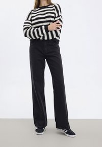 Jeans neri a vita alta e a gamba larga abbinati a un maglione a righe bianche e nere in maglia, con scollatura e polsini a coste. Calzature casual.