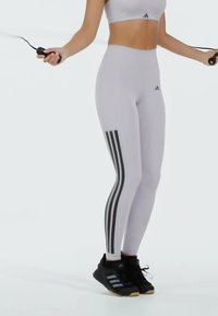 Leggings de entrenamiento blancas con tres rayas verticales negras, combinadas con zapatillas deportivas negras. La parte superior es un crop top blanco a juego.